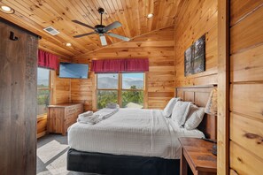 A wooden cabin bedroom with a bed, a TV, and a window with a mountain view.
