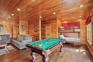 L’intérieur d’un chalet en bois comprend une table de billard, un canapé, des lits superposés et une cheminée.