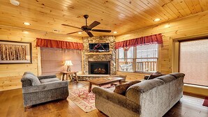 A cozy cabin interior with a stone fireplace, wooden walls, and a ceiling fan.