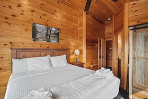 Un dormitorio de cabaña de madera con una cama, una mesita de noche, una lámpara y un cuadro en la pared.
