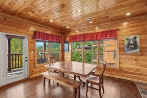 A wooden cabin interior with a dining table, benches, and a view of the outdoors through large windows. - A Breathtaking Smoky Mountain Escape w/ Hot Tub (Gatlinburg)