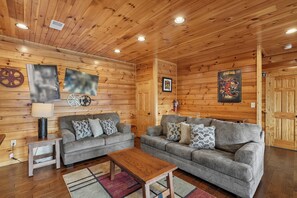 Ein gemütliches Blockhaus-Interieur mit zwei grauen Sofas, einem Holztisch und einer Holzzahlende mit integrierten Leuchten.