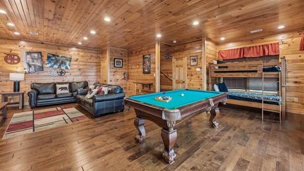 A wooden interior with a pool table, sofas, and a bunk bed.