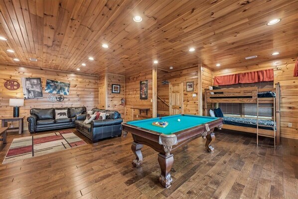 A wooden interior with a pool table, sofas, and a bunk bed.