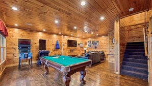 Un interior de madera con mesa de billar, zona de estar y una escalera.