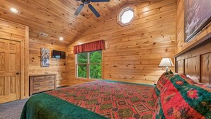 A wooden cabin bedroom with a bed, a window, a ceiling fan, and a dresser.