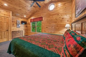 Une chambre à coucher dans une cabane en bois, avec un lit, une fenêtre, un ventilateur de plafond et une commode.