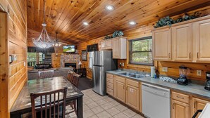 A wooden cabin interior with a dining area, kitchen, and a fireplace.