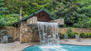 A stone building with a waterfall feature, a pool, and lounge chairs.