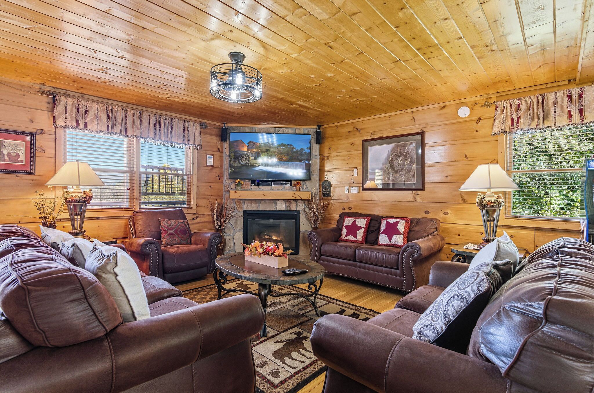 A cozy log cabin interior with leather sofas, a fireplace, a television, and a stone fireplace surround.