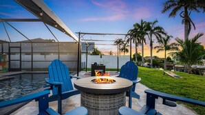 Ein Garten mit Feuerstelle, blauen Adirondack-Stühlen, Schwimmbecken und einer Pergola.
