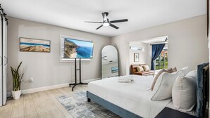 Ein modernes Schlafzimmer mit einem großen Bett, einem Deckenventilator, einem Fernseher und Blick ins Freie.