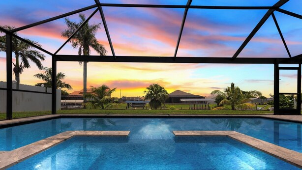 Ein Swimmingpool mit Sonnenuntergangsblick, umgeben von Palmen und einem klaren Himmel.