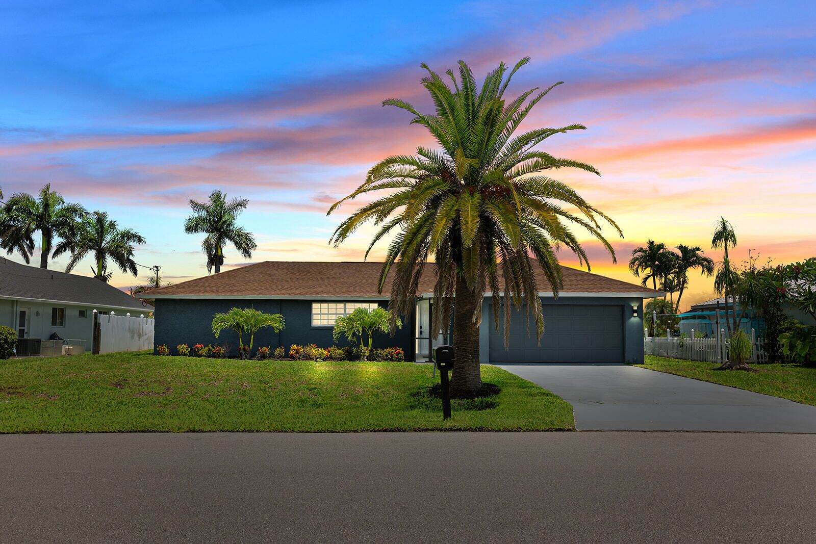 Una casa residencial con césped cuidado, una palmera y un garaje.