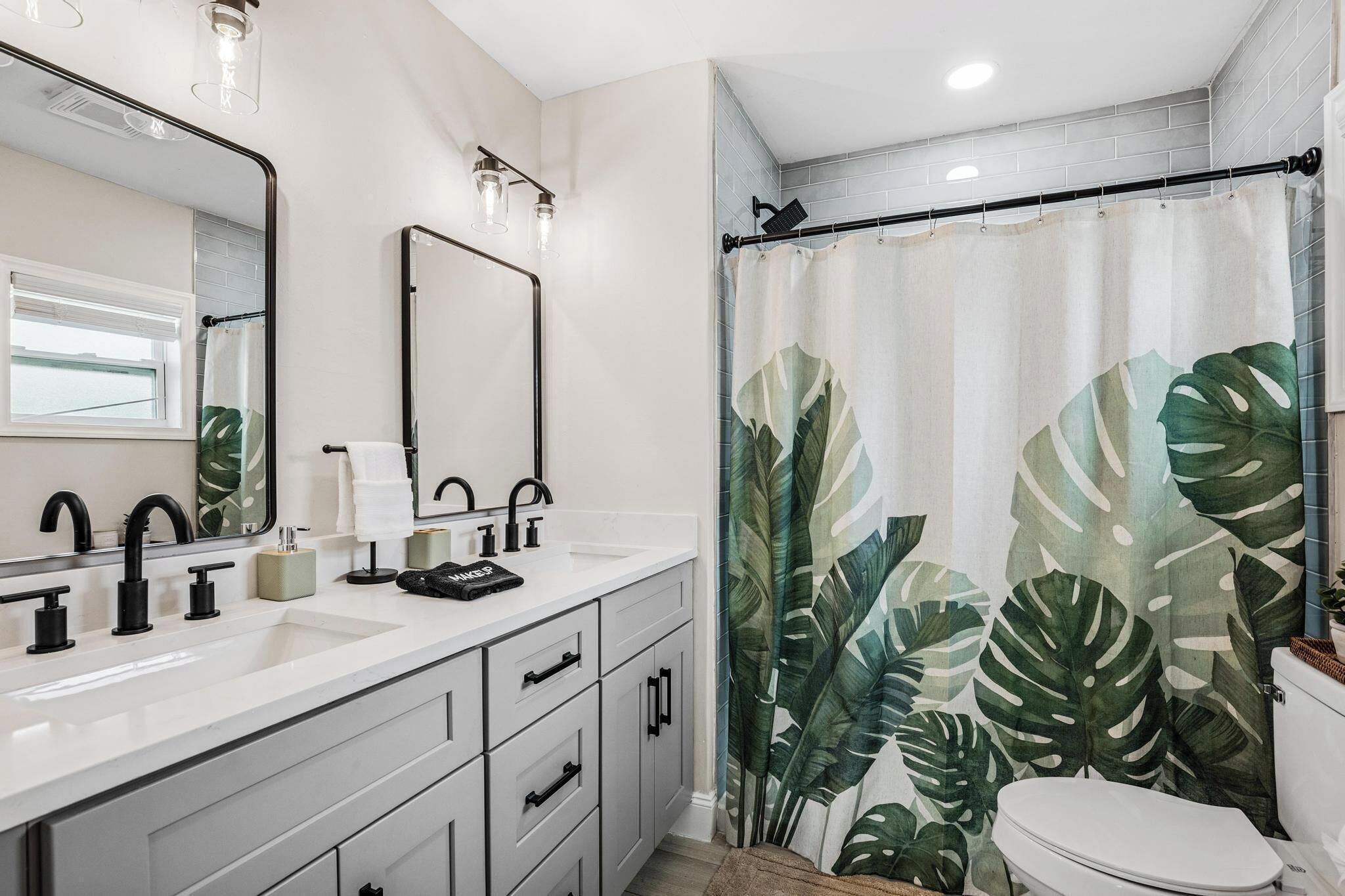 A bathroom with a white sink, black faucets, a mirror, and a shower curtain with a tropical leaf pattern.