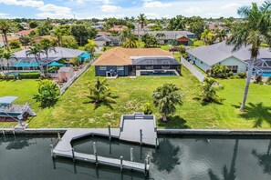 A residential area with a house featuring a large deck, a swimming pool, and a dock with a boat. - Pool, Spa & Dock Modern Canal-Front Escape (Cape Coral)