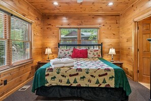 A wooden cabin bedroom with a bed, two bedside lamps, a window, and a door.