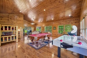 A spacious room with wooden walls and ceiling, a pool table, a foosball table, and a sofa.