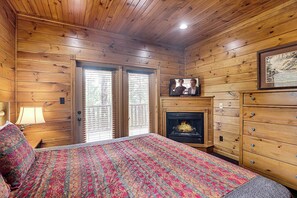 Une pièce de style cabane en bois, comprenant un lit, une cheminée, un téléviseur et une commode.