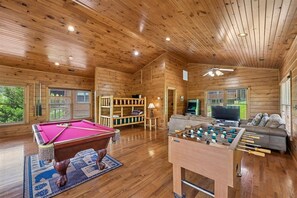A wooden interior with a pool table, foosball table, and a sofa.