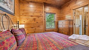 A wooden cabin bedroom with a bed, dresser, and a window with blinds. - Relaxing Smoky Mtn. Getaway w/Views & Family Fun! (Gatlinburg)