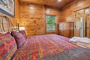 A wooden cabin bedroom with a bed, dresser, and a window with blinds.