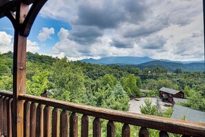 A wooden balcony railing overlooking a lush green landscape with a mountain range in the distance.