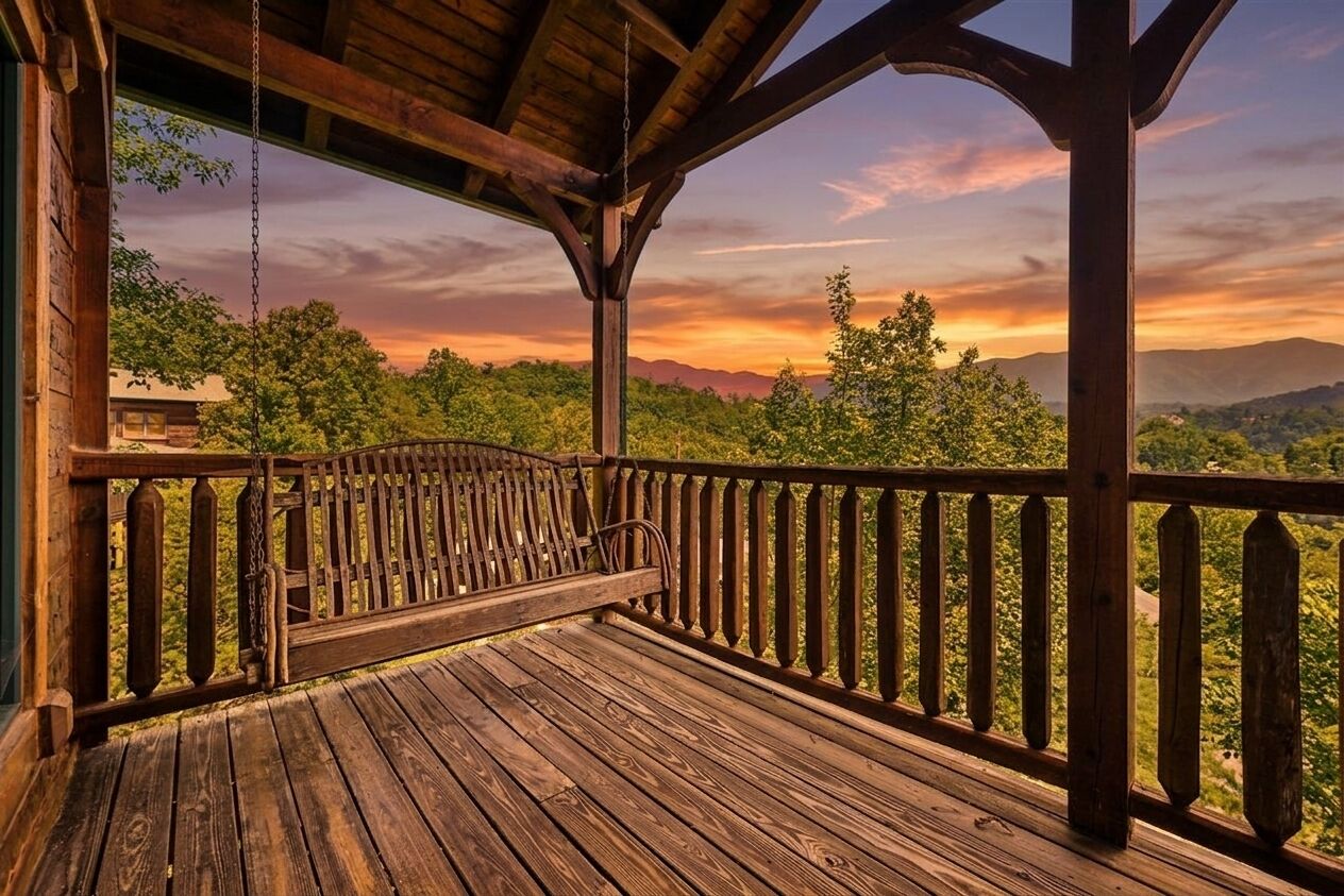 A wooden deck with a swing, overlooking a forested landscape with mountains in the distance.