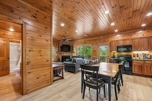A wooden cabin interior with a dining area, kitchen, and a fireplace.