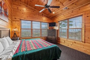 Une chambre dans une cabane en bois, avec un lit, un ventilateur de plafond, une commode et de grandes fenêtres.