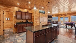 A wooden cabin interior with a kitchen, dining area, and a pool table.