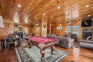Un intérieur en bois avec une table de billard, des canapés et une cheminée.