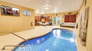 An indoor swimming pool with a lounge area, a fire extinguisher, and a television on the wall.