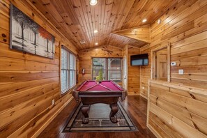 A wooden interior with a pool table, wooden walls, and a television.