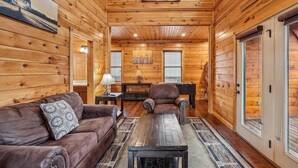 Ein Blockhaus-Interieur mit Sofa, Sessel, Couchtisch und Bildern an den Wänden.