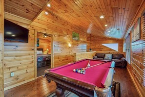 A wooden cabin with a pool table, a sofa, and a television.