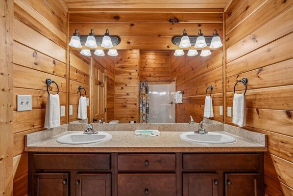 A wooden cabin-style bathroom with two sinks, a mirror, and overhead lighting.