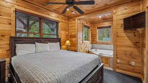 Eine Holzhütte mit einem Bett, einem Deckenventilator, einem Fenster, einem Waschbecken und einem Fernseher.