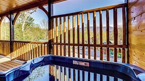 Eine Holzterrasse mit Whirlpool, Holzgeländern und Blick auf Bäume und Berge.