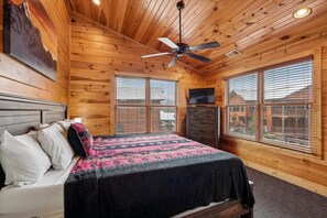 Camera da letto in una baita di legno con un letto, una ventola a soffitto, un comò e una TV.