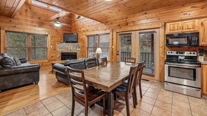Ein Holzblockbau-Innenraum mit Esstisch, Stühlen, Sofas, einem Kamin, einem Fernseher und einer Küchenzeile.