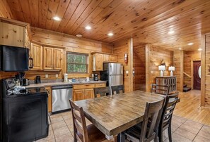 Cocina estilo cabaña con paredes de madera, una isla central y una mesa de comedor con sillas.