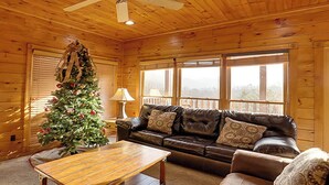 A cozy cabin interior with a wooden ceiling, a leather sofa, a coffee table, and a Christmas tree. - Tranquil Rustic Cabin w/ Game Area & Hot Tub (Gatlinburg)