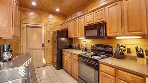 A kitchen with wooden cabinets, a refrigerator, a microwave, a stove, and a coffee maker. - Tranquil Rustic Cabin w/ Game Area & Hot Tub (Gatlinburg)