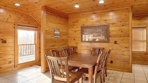 A wooden cabin interior with a dining table and chairs, wooden walls, and a framed picture on the wall. - Tranquil Rustic Cabin w/ Game Area & Hot Tub (Gatlinburg)