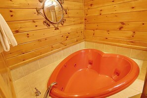 L’intérieur d’un chalet en bois comprend une grande baignoire ovale, un mur en bois orné d’un miroir et un sol carrelé.
