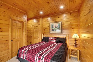 Une chambre dans une cabane en bois, avec un lit, une table de chevet et un tableau accroché au mur.