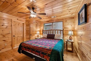 Une chambre à coucher dans un chalet en bois, avec un lit, un ventilateur de plafond, une fenêtre et une table de chevet avec une lampe.