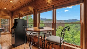 Une pièce aux murs lambrés, équipée d’une table de billard, d’un barbecue et de grandes fenêtres offrant une vue sur les montagnes.