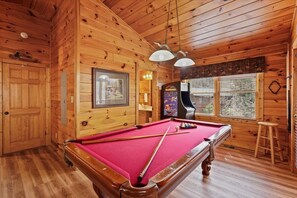 A wooden cabin with a pool table, a framed picture, and a pinball machine.